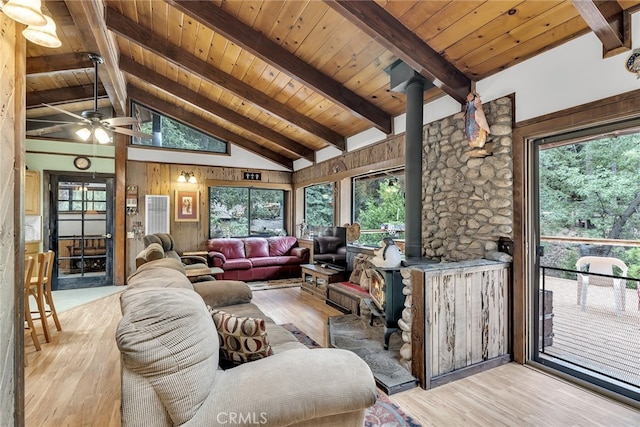 living room with light wood-type flooring, a wood stove, and high vaulted ceiling