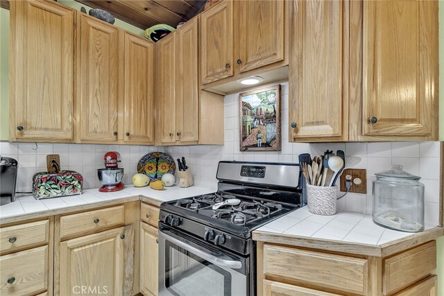 kitchen with stainless steel range with gas cooktop, backsplash, light brown cabinets, and tile countertops