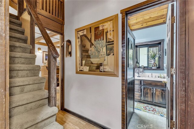 hall with light hardwood / wood-style flooring, wood ceiling, and sink