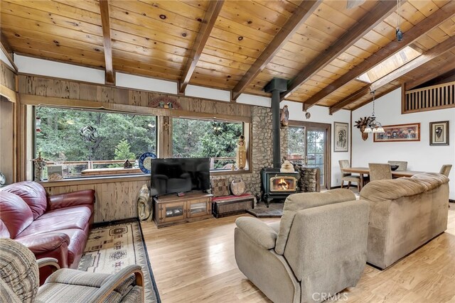 living room with wood ceiling, light hardwood / wood-style floors, a wood stove, beam ceiling, and a skylight