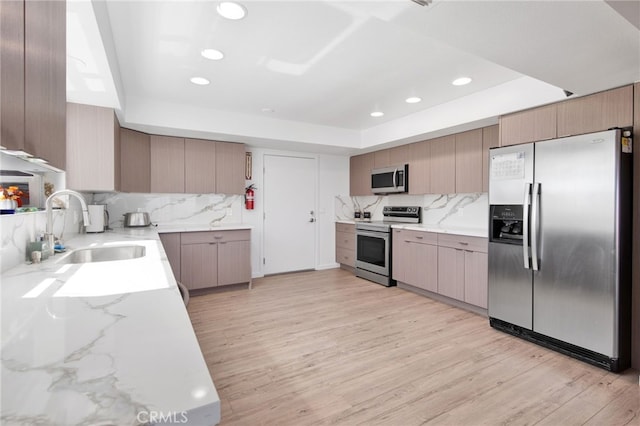 kitchen with sink, tasteful backsplash, light hardwood / wood-style flooring, a tray ceiling, and appliances with stainless steel finishes