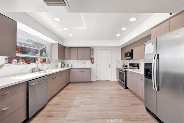 kitchen with light wood-type flooring, sink, stainless steel appliances, backsplash, and light stone countertops