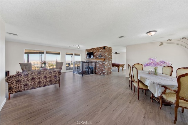 dining room featuring a brick fireplace, wood-type flooring, and a textured ceiling