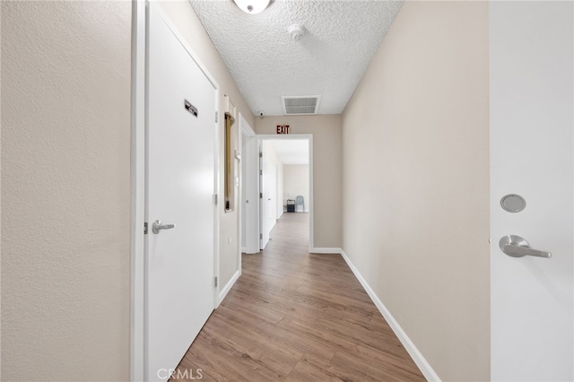 hall with a textured ceiling and light hardwood / wood-style floors