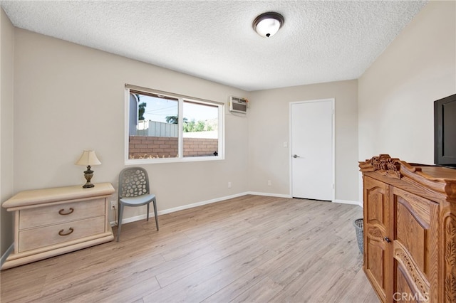 sitting room featuring a textured ceiling, light wood-type flooring, and an AC wall unit