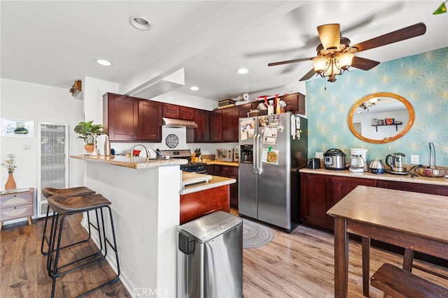 kitchen with appliances with stainless steel finishes, light hardwood / wood-style floors, ceiling fan, and a kitchen breakfast bar