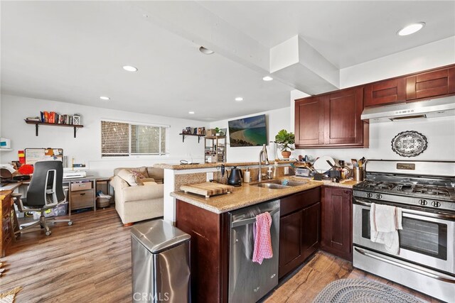 kitchen featuring sink, light stone counters, kitchen peninsula, light hardwood / wood-style floors, and appliances with stainless steel finishes