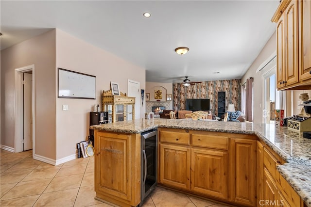 kitchen featuring beverage cooler, kitchen peninsula, light tile patterned floors, light stone countertops, and ceiling fan