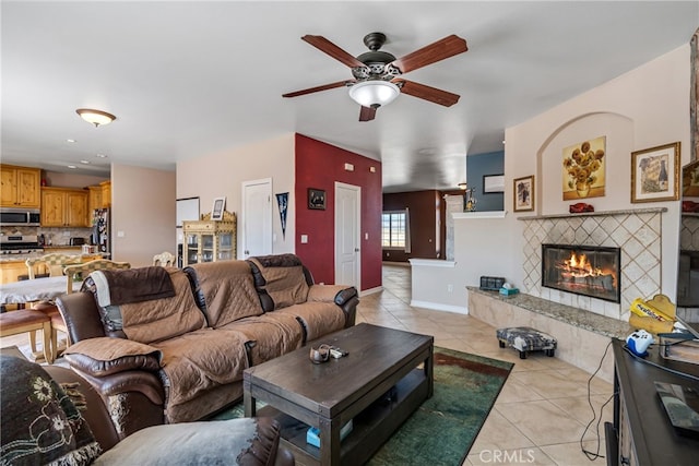 living room with a tiled fireplace, light tile patterned floors, and ceiling fan