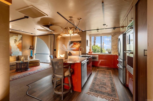 kitchen featuring ceiling fan, a kitchen bar, dark wood-type flooring, wooden counters, and stainless steel appliances