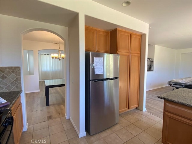 kitchen featuring stove, light tile patterned floors, dark stone counters, and stainless steel refrigerator