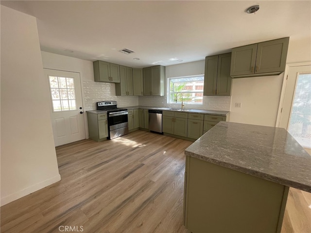 kitchen with green cabinetry, light hardwood / wood-style flooring, stainless steel appliances, and tasteful backsplash