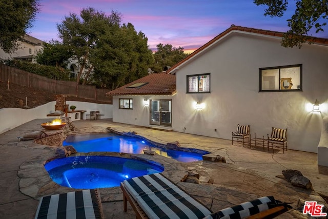 pool at dusk featuring a fire pit, a patio area, and an in ground hot tub