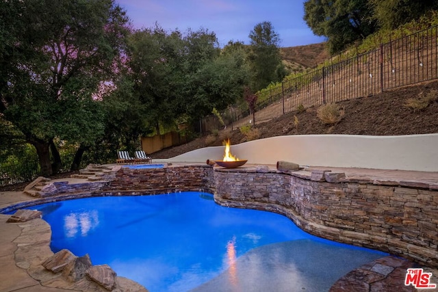 pool at dusk with an in ground hot tub