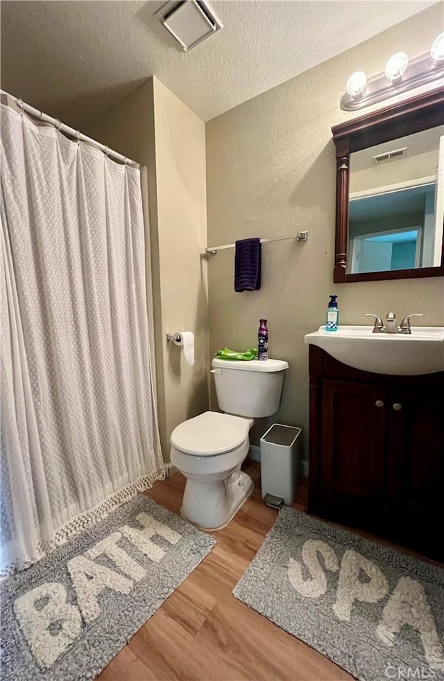 bathroom featuring a textured ceiling, toilet, wood finished floors, and visible vents