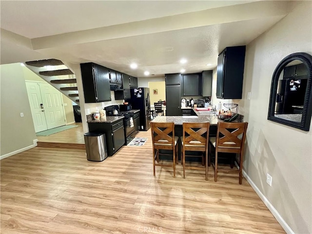 kitchen featuring a breakfast bar area, a sink, dark cabinets, a peninsula, and black appliances