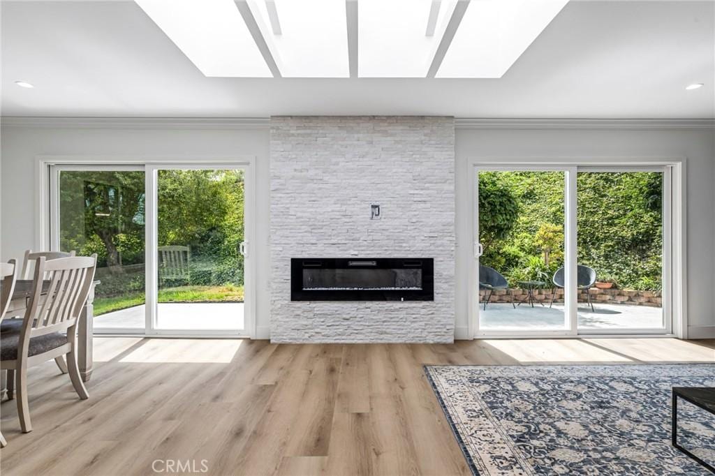 living room with light wood-type flooring, a skylight, a stone fireplace, and a wealth of natural light