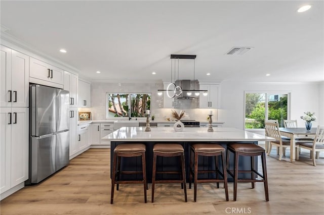 kitchen with decorative light fixtures, white cabinetry, a kitchen island with sink, and stainless steel refrigerator