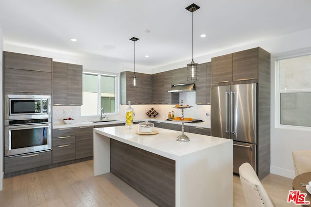 kitchen with a center island, sink, stainless steel appliances, light hardwood / wood-style flooring, and decorative light fixtures