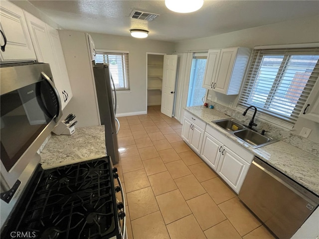 kitchen with white cabinetry, light stone counters, light tile patterned floors, stainless steel appliances, and sink