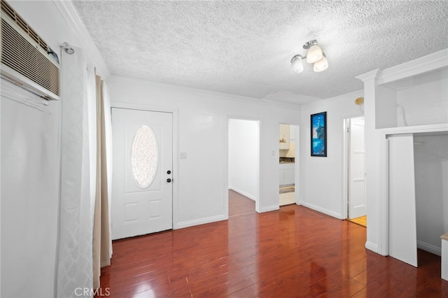 foyer entrance featuring a wall mounted air conditioner, a textured ceiling, crown molding, and dark wood-type flooring