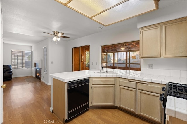 kitchen with tile counters, black dishwasher, stainless steel range oven, and light hardwood / wood-style flooring