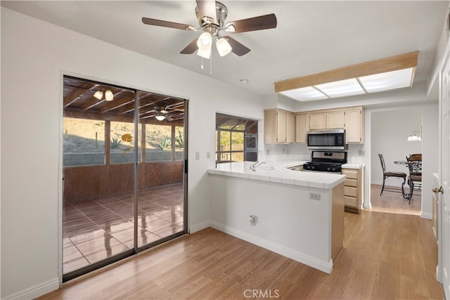 kitchen with kitchen peninsula, stainless steel appliances, tile countertops, ceiling fan, and light hardwood / wood-style flooring