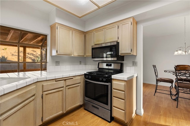 kitchen with stainless steel appliances, light hardwood / wood-style floors, and tile countertops