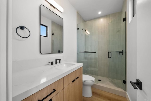 bathroom with wood-type flooring, vanity, toilet, and a shower with door