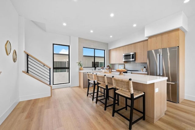 kitchen with appliances with stainless steel finishes, backsplash, a breakfast bar area, a center island, and light hardwood / wood-style flooring