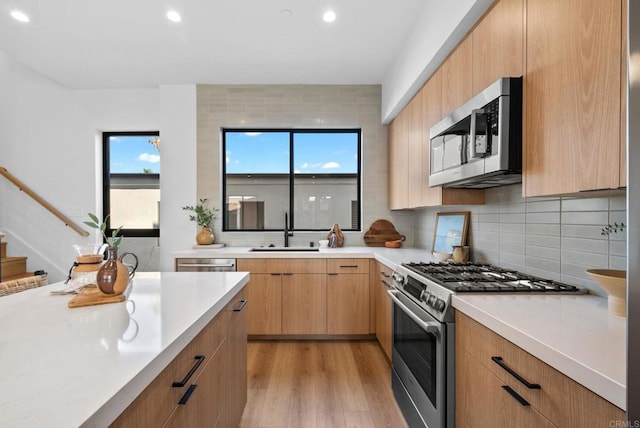 kitchen with sink, tasteful backsplash, appliances with stainless steel finishes, light brown cabinetry, and light hardwood / wood-style floors