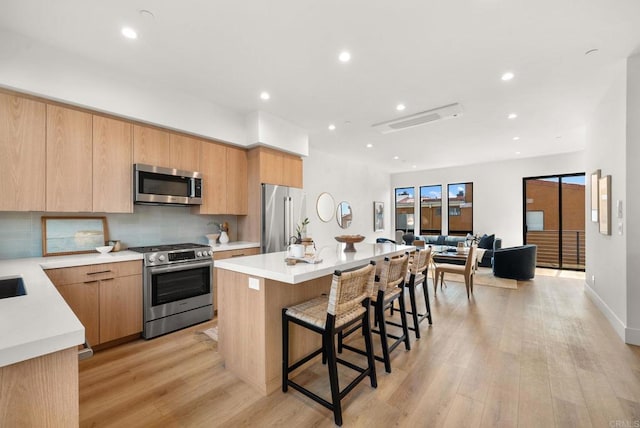 kitchen featuring light wood-type flooring, a kitchen island, a breakfast bar area, and stainless steel appliances