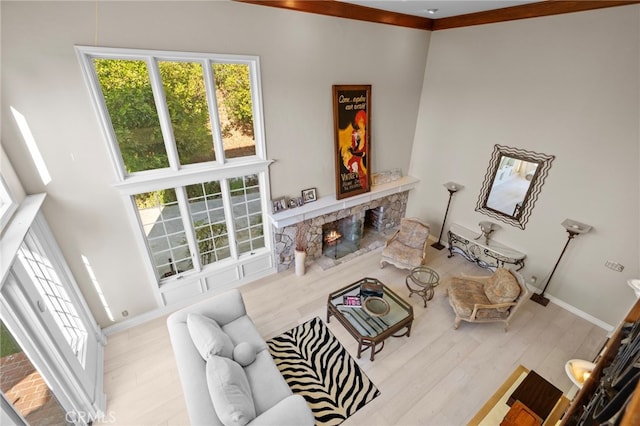 living room featuring light wood-type flooring, a fireplace, a high ceiling, and crown molding