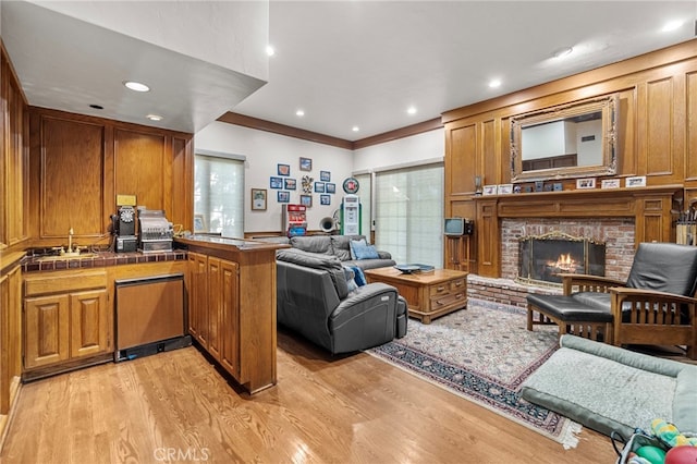 living room with a brick fireplace, ornamental molding, and light hardwood / wood-style floors