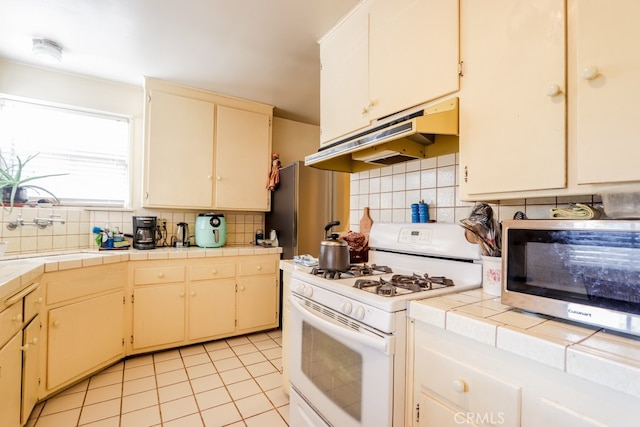 kitchen featuring tasteful backsplash, light tile patterned floors, white range with gas cooktop, tile counters, and sink