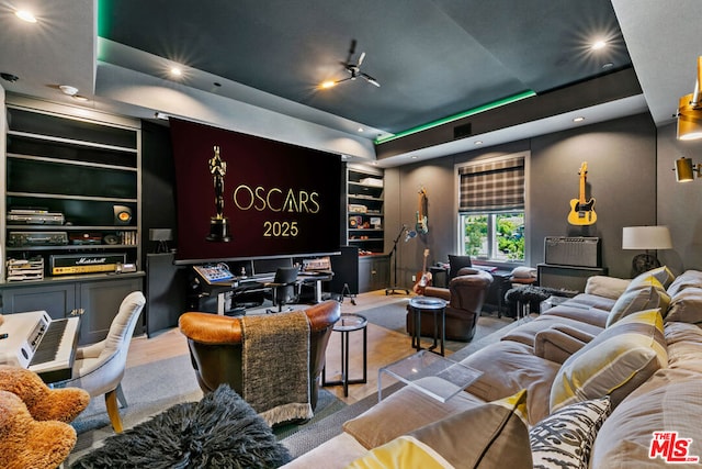 cinema featuring built in shelves, a tray ceiling, and light wood-type flooring