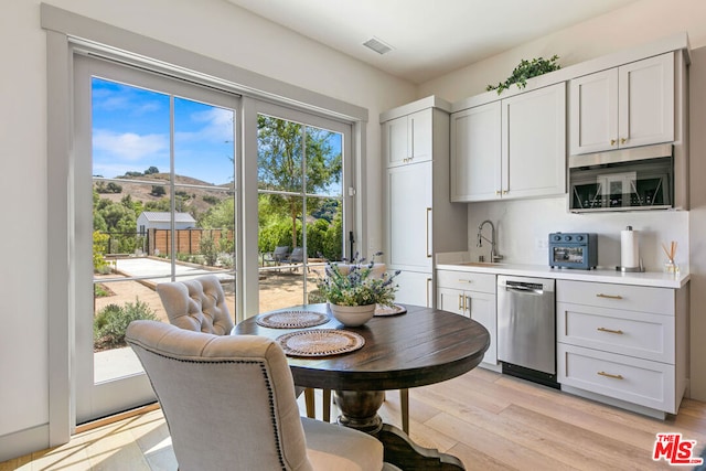 kitchen with sink, stainless steel dishwasher, white cabinets, and light hardwood / wood-style flooring