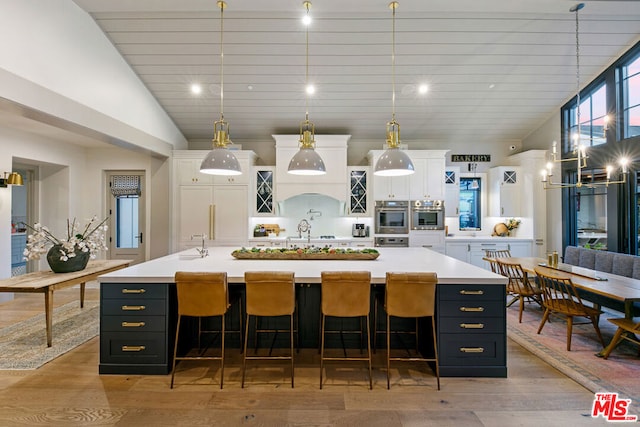 kitchen featuring a large island with sink, white cabinetry, and hanging light fixtures