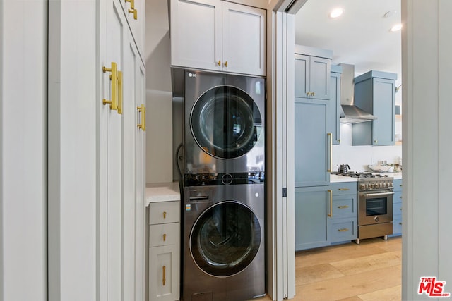 clothes washing area featuring cabinets, stacked washer / drying machine, and light wood-type flooring