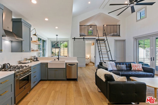 kitchen with decorative light fixtures, stainless steel appliances, a barn door, light hardwood / wood-style floors, and wall chimney range hood