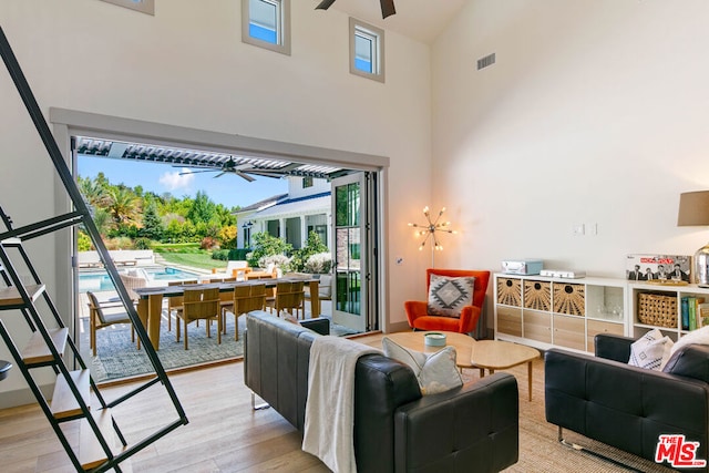 living room featuring a towering ceiling, light hardwood / wood-style floors, and ceiling fan