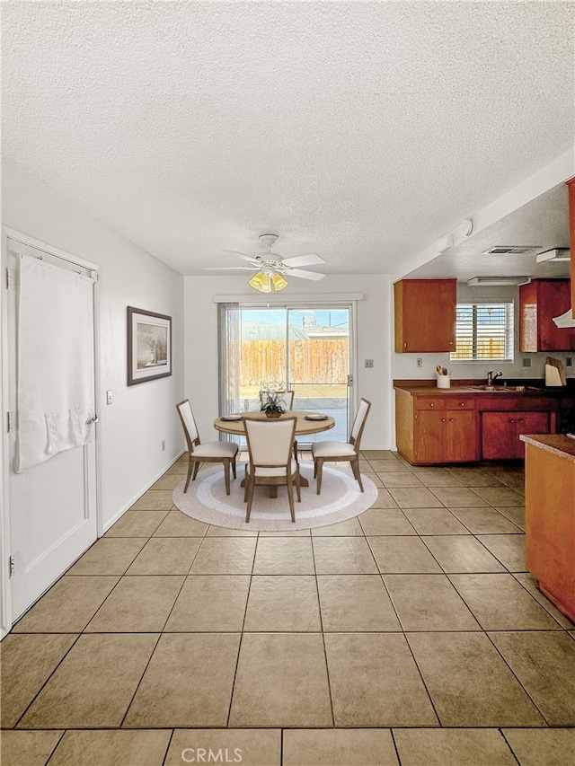 tiled dining area featuring ceiling fan, a textured ceiling, sink, and a healthy amount of sunlight