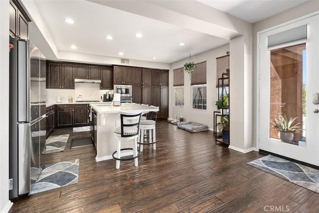 kitchen with a kitchen island, dark brown cabinets, stainless steel appliances, dark hardwood / wood-style floors, and a kitchen breakfast bar