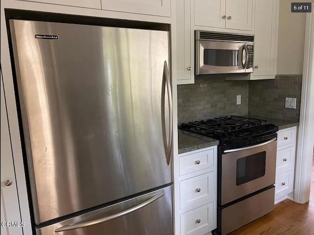 kitchen featuring backsplash, white cabinetry, hardwood / wood-style flooring, appliances with stainless steel finishes, and dark stone countertops