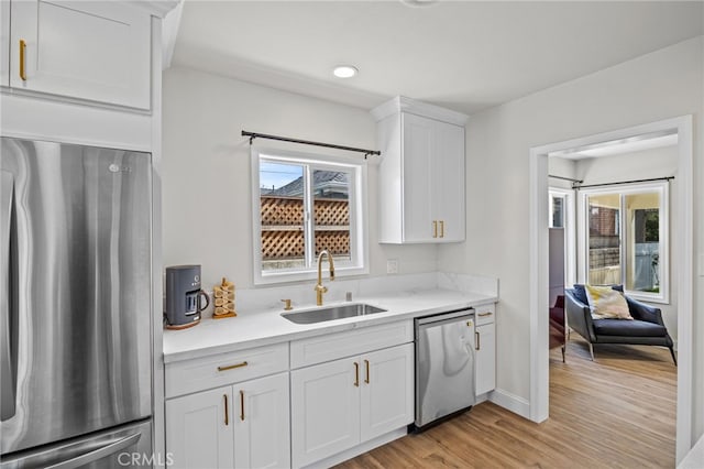 kitchen featuring stainless steel appliances, white cabinets, light wood-type flooring, and sink