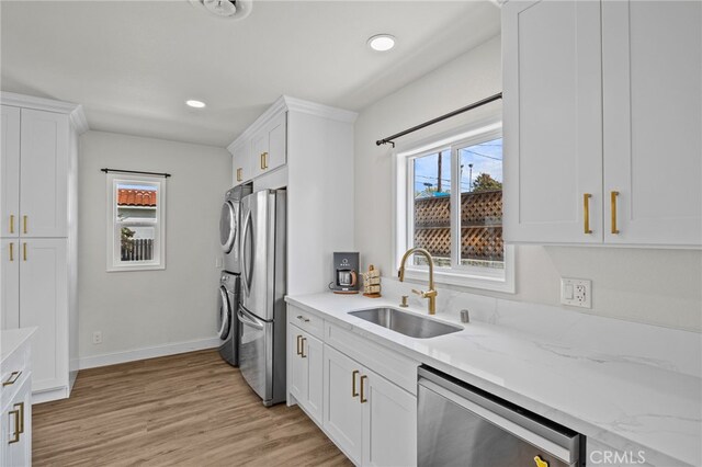 kitchen featuring stacked washer and clothes dryer, stainless steel appliances, light hardwood / wood-style floors, and white cabinets