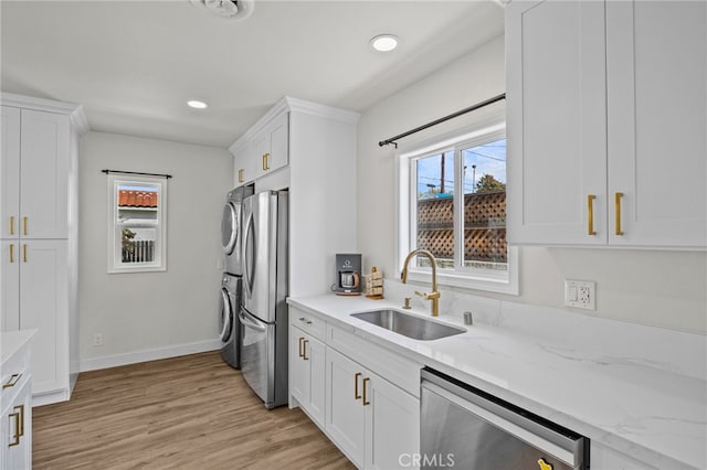 kitchen with stacked washer and dryer, appliances with stainless steel finishes, a sink, light wood-style flooring, and white cabinetry