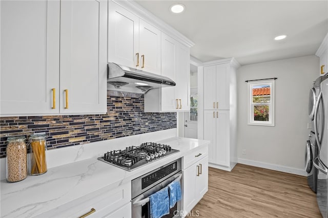 kitchen with light hardwood / wood-style floors, stacked washer / drying machine, white cabinets, appliances with stainless steel finishes, and light stone countertops