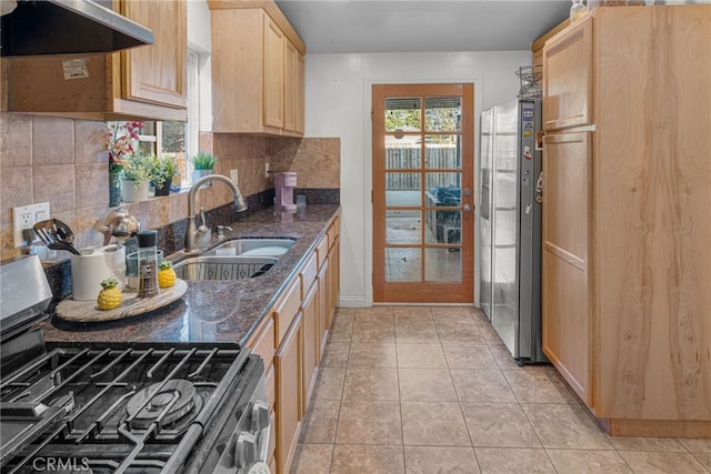 kitchen with appliances with stainless steel finishes, light brown cabinetry, dark stone counters, sink, and extractor fan