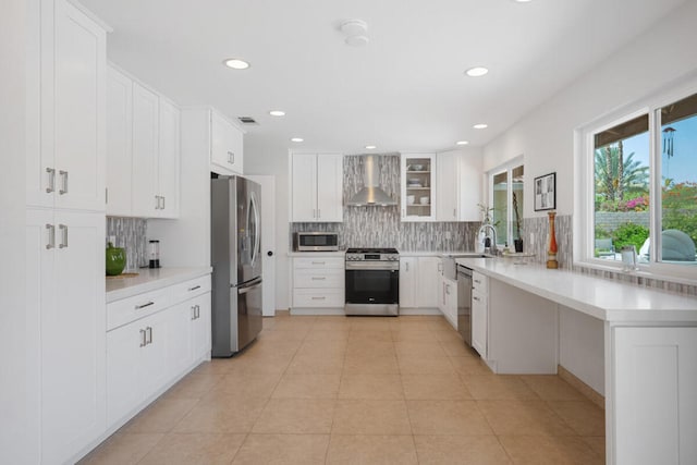 kitchen with light tile patterned flooring, white cabinetry, tasteful backsplash, stainless steel appliances, and wall chimney range hood